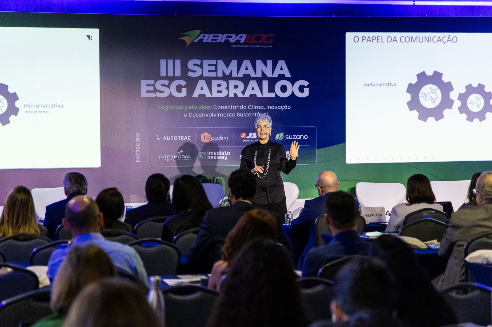 Vania Bueno no palco de um evento, falando para uma plateia